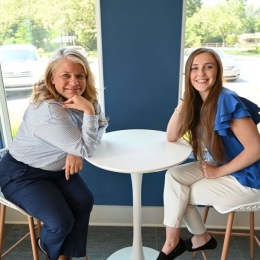 Smiles that say, 'we’ve got you covered! two women sitting at a table posing