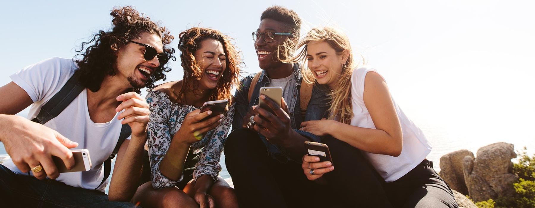 a group of friends sit outside laughing over their cell phones