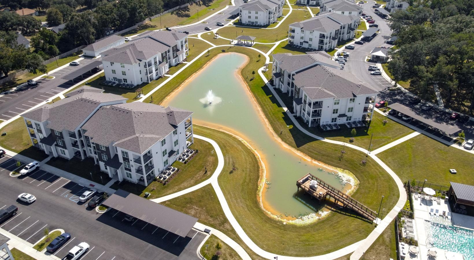 Settle into comfort at The Flats at East Bay aerial view of a large building and a pond and a pool