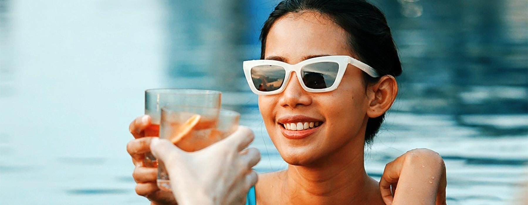 a woman in a pool holding a drink and a glass